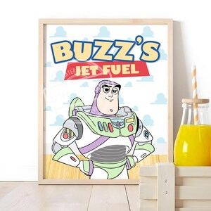 May include: A framed print featuring a cartoon illustration of Buzz Lightyear in a white, green, and purple space suit. The text BUZZ'S JET FUEL is printed in blue and white above the character against a background of light blue clouds.
