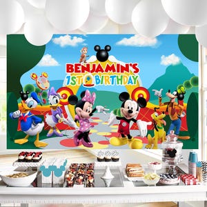 May include: A vibrant backdrop with Disney characters Mickey Mouse, Minnie Mouse, Donald Duck, Daisy Duck, Goofy, and Pluto. The banner says "Benjamin's 1st Birthday". White balloons are above a table with party food and decorations.