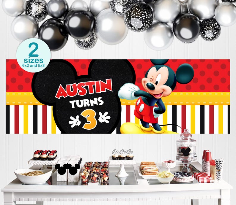 May include: A party banner featuring Mickey Mouse with the text "Austin Turns 3". The banner has a red background with white polka dots, yellow and black stripes, and a black Mickey Mouse head. The image also includes balloons and a table with desserts.