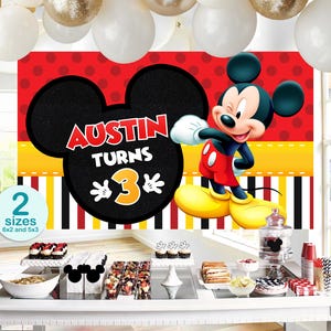 May include: A colorful birthday party backdrop featuring Mickey Mouse. The backdrop has a red background with black polka dots and a large Mickey Mouse head with the text "Austin Turns 3". The image also includes party decorations and treats.