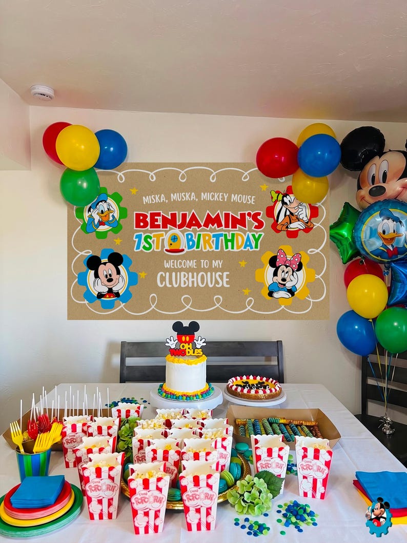 Puede incluir: Decoraci&oacute;n de fiesta de cumplea&ntilde;os con tem&aacute;tica de Mickey Mouse. Incluye una pancarta que dice "Benjamin's 1st Birthday", globos, una tarta y cajas de palomitas. Los colores principales son rojo, amarillo y azul.