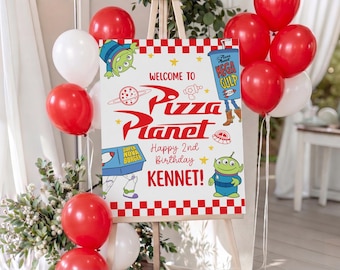 May include: A rectangular white sign with a red and white chequered border featuring the text Welcome to Pizza Planet Happy 2nd Birthday KENNET. The sign includes illustrations of green three-eyed aliens, a blue burger box, and a blue drink cup.