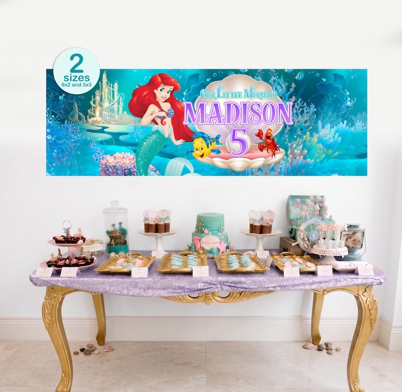 Puede incluir: Una mesa de fiesta con una pancarta con Ariel de La Sirenita, con el nombre "Madison" y el n&uacute;mero "5". La mesa est&aacute; decorada con postres, incluyendo una tarta, cupcakes y otras golosinas, todo con tem&aacute;tica de sirena.