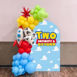 May include: A balloon arch featuring a blue backdrop with white clouds and the text TWO INFINITY & BEYOND. The arch includes lime green, yellow, red, and light blue balloons, white balloons with black cow print, and a silver rocket ship balloon.