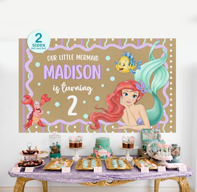 K&ouml;nnte beinhalten: Ein Geburtstagsbanner mit der kleinen Meerjungfrau Arielle, mit dem Text "Our Little Mermaid Madison is turning 2." Das Banner hat einen braunen Hintergrund mit lila und t&uuml;rkisfarbenen Akzenten. Ein Tisch ist mit Desserts gedeckt.