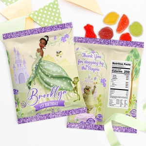 Op de afbeelding: Paarse en groene feestzakjes met een prinsesfiguur en een kikkerfiguur. De zakjes hebben een glitterafwerking en er staat "Brooklyn 1e verjaardag" en "Bedankt voor het langs komen bij de Bayou" op.