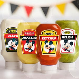 May include: Four condiment bottles: mayo, mustard, ketchup, and relish. Each bottle has a Mickey Mouse label. The mayo bottle is off-white, mustard is yellow, ketchup is red, and relish is green. A banner of red, yellow, and black flags is in the background.