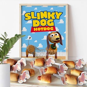 May include: A framed poster with the words "SLINKY DOG HOTDOG" against a blue sky background with white clouds. The poster features a cartoon Slinky Dog character. A tray of hot dogs with Slinky Dog cutouts is in front of the poster.