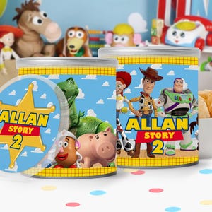 May include: Two cylindrical containers featuring Toy Story characters including Woody, Buzz Lightyear, Jessie, Rex, Mr. Potato Head, and Hamm. The labels display the text ALLAN STORY 2 on a yellow sheriff badge graphic against a blue sky background.