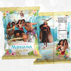 May include: A colorful party favor bag featuring characters from the animated movie Moana. The bag is decorated with a blue ocean background, tropical flowers, and a gold glitter border. The text "Our Wayfinder Moana turns two" is printed on the front of the bag.