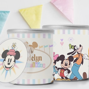 May include: Two cylindrical containers with lids, featuring Disney characters. One has a Mickey Mouse design with the text "Madelyn Birthday". The other container has Mickey, Minnie, and Goofy. Pastel stripes and pennants decorate the background.