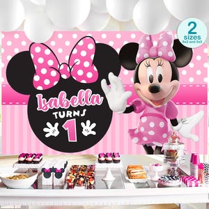 Op de afbeelding: Een verjaardagsfeestdecoratie met Minnie Mouse-thema. De achtergrond toont Minnie's silhouet, een roze strik met witte stippen en de tekst "Isabella Turns 1". De tafel is gedekt met lekkernijen en decoraties.