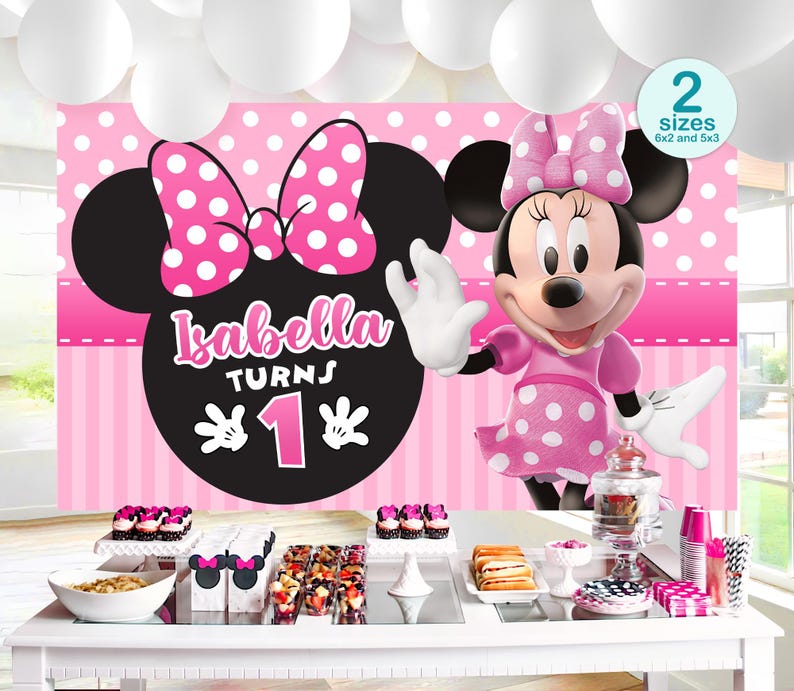Op de afbeelding: Een verjaardagsfeestdecoratie met Minnie Mouse-thema. De achtergrond toont Minnie's silhouet, een roze strik met witte stippen en de tekst "Isabella Turns 1". De tafel is gedekt met lekkernijen en decoraties.