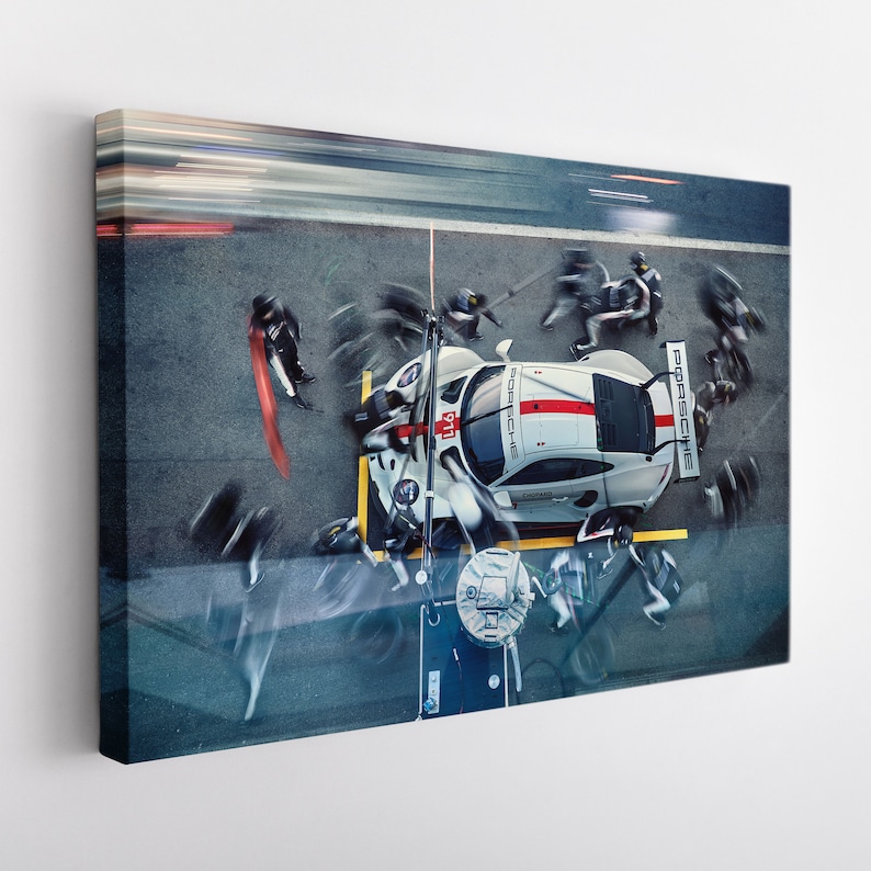 May include: A white and red race car with the word "Porsche" on the side is being worked on by a pit crew. The car is on a racetrack with a blurred background.