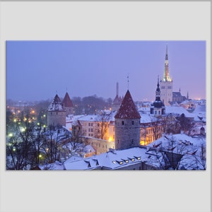 May include: A snowy cityscape with a tall, pointed church spire and several smaller towers. The buildings are lit up with warm lights, and the sky is a soft blue.