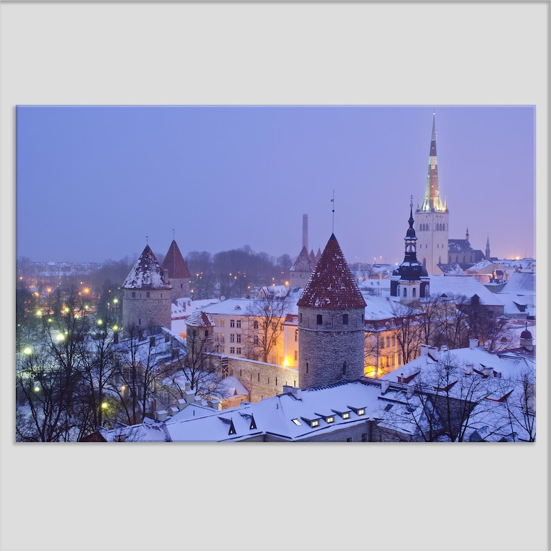 May include: A snowy cityscape with a tall, pointed church spire and several smaller towers. The buildings are lit up with warm lights, and the sky is a soft blue.