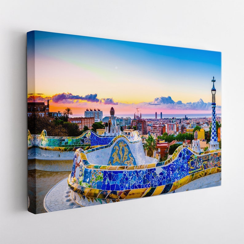 May include: A colorful mosaic bench overlooking a cityscape at sunset. The bench is made of blue, yellow, and white tiles. The city skyline is in the background, with the sea visible in the distance.