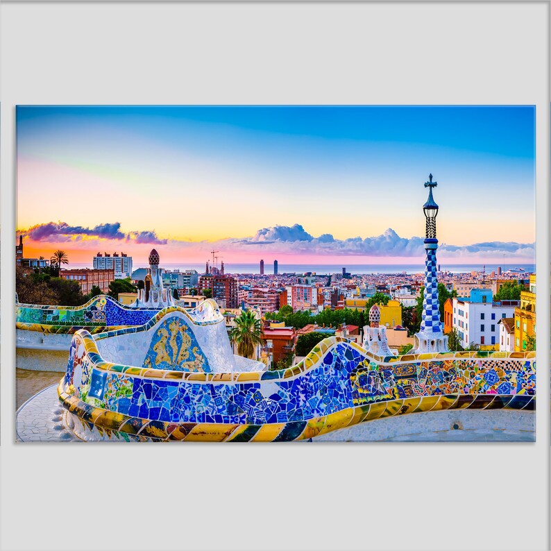 May include: A colorful mosaic bench with a view of the Barcelona skyline at sunset. The bench is decorated with blue, yellow, and green tiles. The city skyline is in the background, with the Mediterranean Sea in the distance.