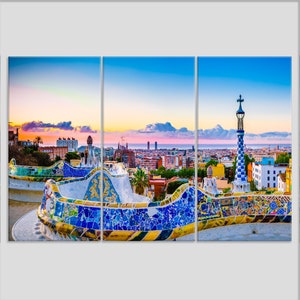 May include: A panoramic view of Barcelona, Spain, at sunset, with a mosaic tiled bench in the foreground. The city skyline is visible in the distance, with the Mediterranean Sea in the background.