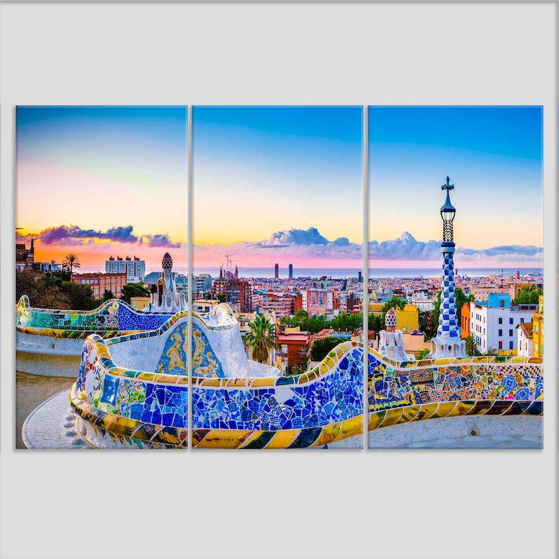 May include: A panoramic view of Barcelona, Spain, at sunset, with a mosaic tiled bench in the foreground. The city skyline is visible in the distance, with the Mediterranean Sea in the background.