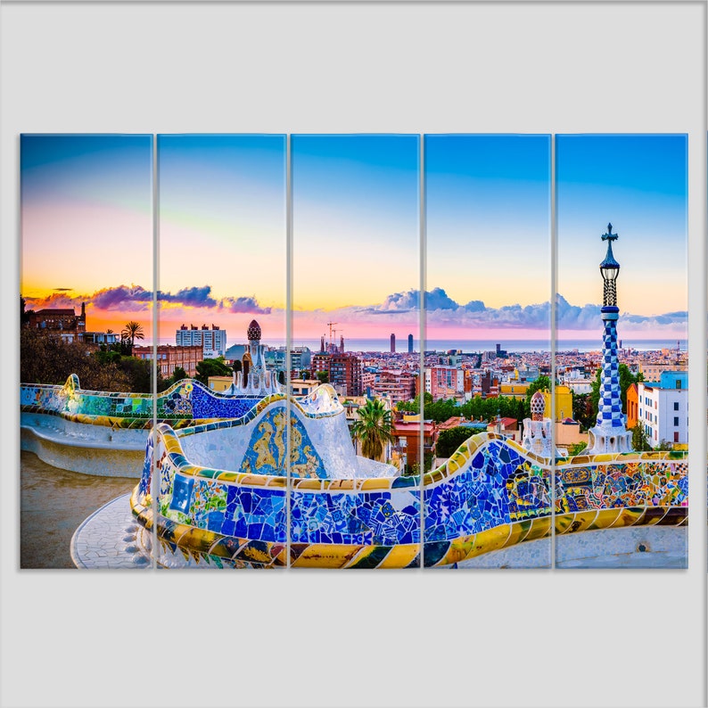 May include: A panoramic view of Barcelona, Spain, with a colorful mosaic bench in the foreground. The city skyline is visible in the background, with the Mediterranean Sea in the distance. The sky is a vibrant blue with pink and orange hues.