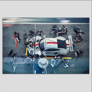 May include: A white Porsche race car with red and black accents is being serviced by a pit crew. The car is on a track with a yellow line and the crew members are blurred as they move around the car.