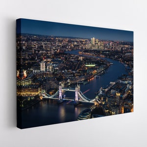 May include: An aerial view of Tower Bridge in London at night. The bridge is illuminated and the city lights are reflected in the River Thames.