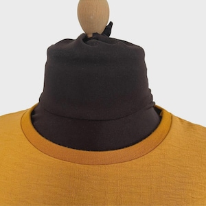 Puede incluir: Una camiseta de color amarillo mostaza con cuello redondo acanalado que presenta un calentador de cuello o cuello alto de tela marr&oacute;n oscuro ajustado, creando una apariencia de capas con colores y texturas contrastantes.