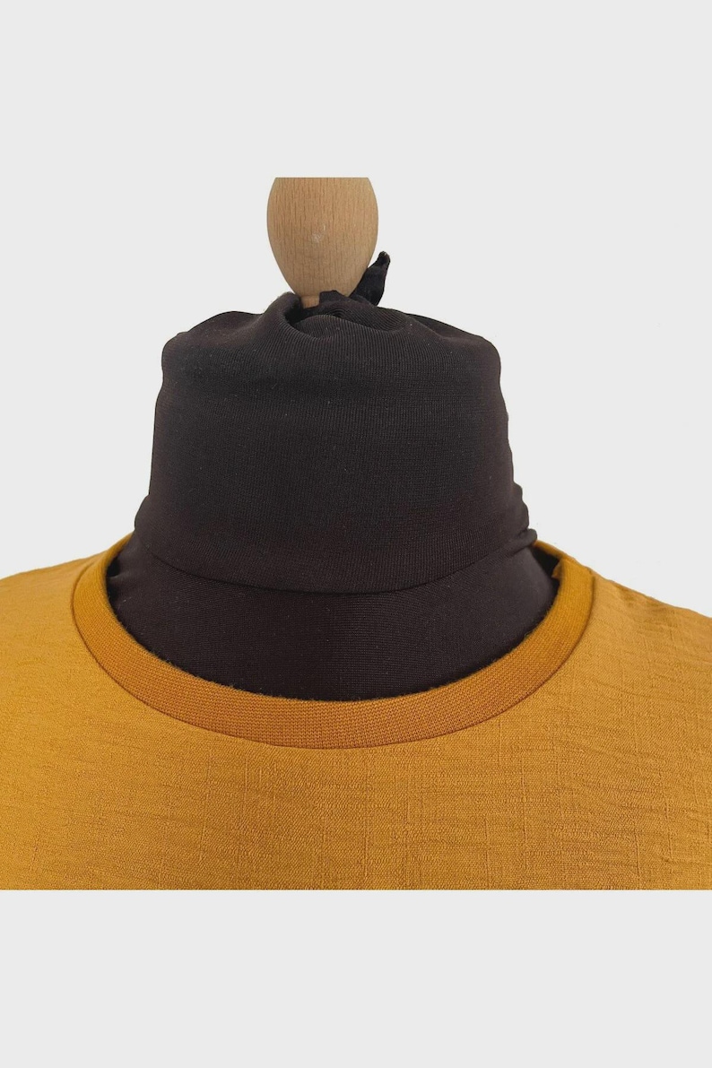 Puede incluir: Una camiseta de color amarillo mostaza con cuello redondo acanalado que presenta un calentador de cuello o cuello alto de tela marr&oacute;n oscuro ajustado, creando una apariencia de capas con colores y texturas contrastantes.