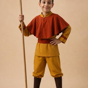 Puede incluir: Un disfraz compuesto por una t&uacute;nica de color amarillo mostaza con mangas largas, una capa de color &oacute;xido, un cintur&oacute;n a juego, pantalones de color amarillo mostaza, polainas de color marr&oacute;n oscuro y zapatillas claras, con un bast&oacute;n de madera.
