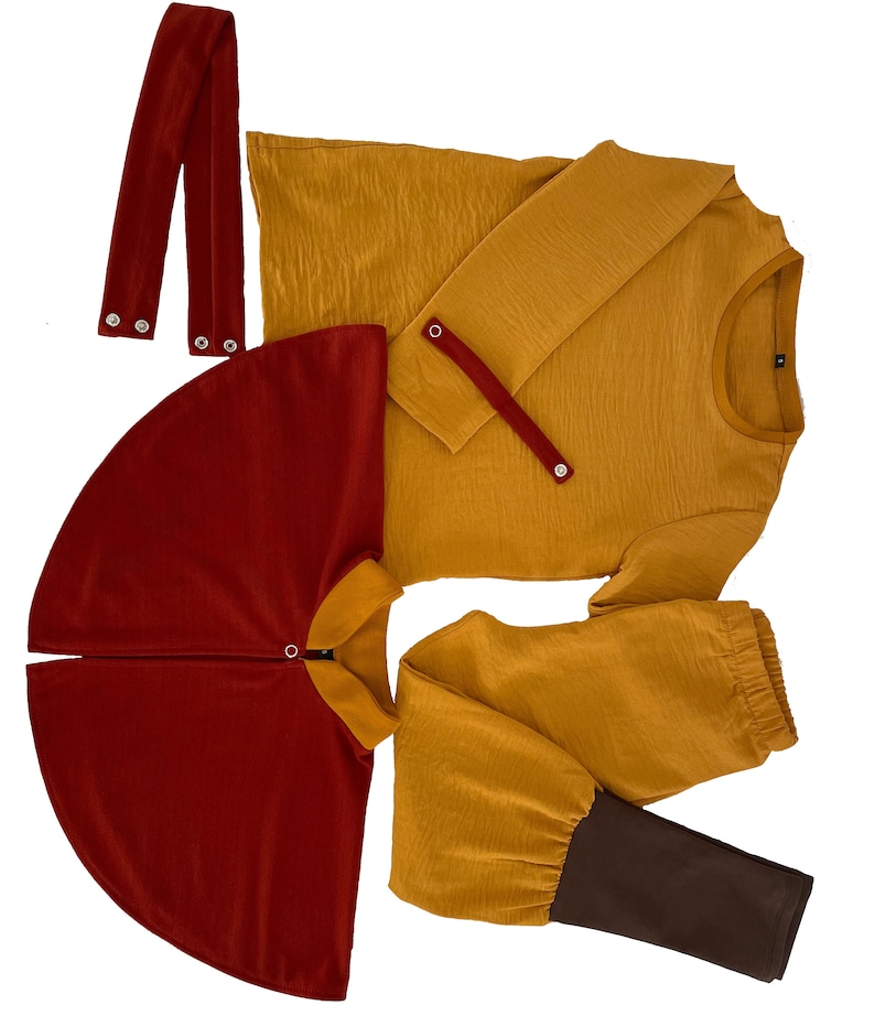 Puede incluir: Una camisa de manga larga color amarillo mostaza con una tira de bot&oacute;n a presi&oacute;n, una capa rojo oscuro con cuello y cierre a presi&oacute;n, un pantal&oacute;n amarillo mostaza con pu&ntilde;os marr&oacute;n oscuro y dos tiras de tela rojo oscuro con botones a presi&oacute;n.