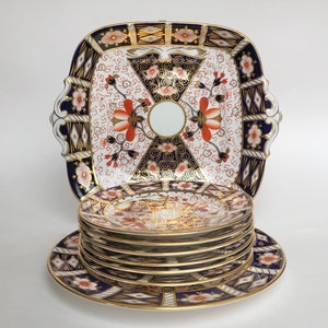 May include: A set of 9 vintage ceramic plates in a blue, red, and gold floral pattern. The plates are stacked with a square serving plate on top.
