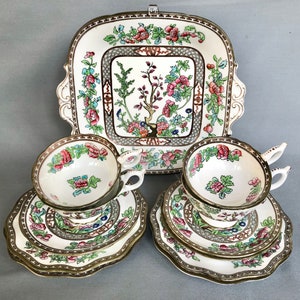 May include: A vintage tea set featuring floral patterned cups, saucers and a cake plate. The set is white with a green, pink and gold floral design.