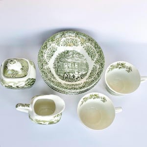 Peut inclure: Ensemble de vaisselle en céramique verte et blanche vintage. Comprend des bols, des tasses, une crémière et un sucrier avec couvercle. Les bols présentent un motif de paysage, les tasses et le sucrier des motifs floraux.