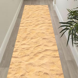 Op de afbeelding: Een rechthoekig loperkleed met een zandtextuurontwerp. Het kleed is voornamelijk beige met een patroon van gerimpeld zand, waardoor een strandachtige esthetiek ontstaat. Het kleed is in een gang geplaatst.