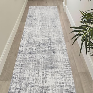 May include: A long, rectangular runner rug featuring a distressed, abstract pattern in shades of white, light gray, and dark charcoal gray. The design consists of textured, weathered-looking horizontal and vertical lines across the surface.