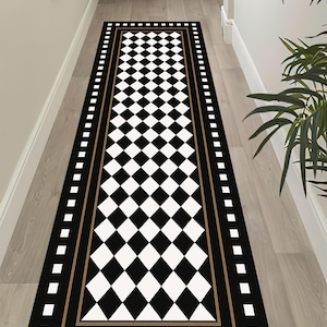 May include: A long, rectangular black and white checkered rug with a border of black, gold, and white squares. The rug is placed in a hallway with light-colored walls and flooring. The rug's design is a classic, geometric pattern.
