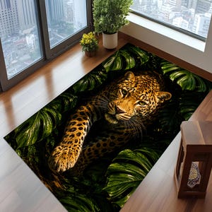 Puede incluir: Una alfombra rectangular con un estampado tridimensional de alta resolución de un leopardo descansando entre exuberantes hojas de monstera de color verde oscuro. El leopardo tiene un pelaje marrón dorado con manchas negras.