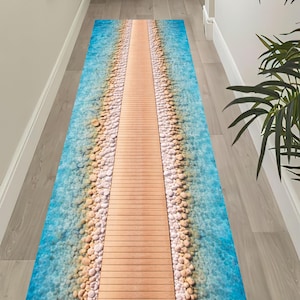 May include: A rectangular rug featuring a beach scene. The design includes a wooden boardwalk flanked by turquoise water and pebbles. The rug is designed to resemble a beach scene, creating a coastal theme.