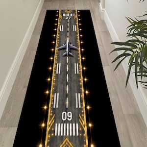 May include: A long rectangular runner rug featuring a high-contrast graphic print of an airport runway at night. The design includes a central gray asphalt strip with white markings, the numbers 09 and 27, yellow runway lights, and an airplane.