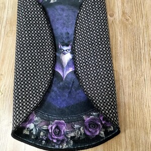 Puede incluir: Una alfombra redonda de color negro y morado con un dise&ntilde;o de murci&eacute;lago y rosas. La alfombra tiene un patr&oacute;n a cuadros en los bordes.
