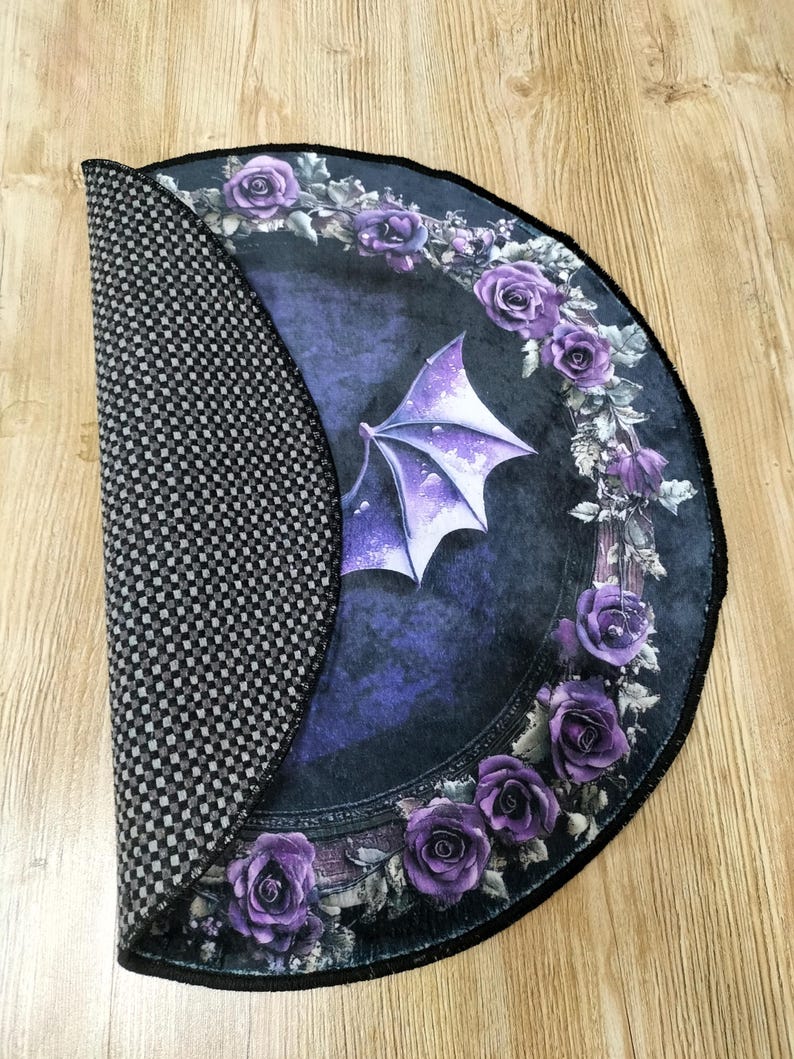 Puede incluir: Una alfombra redonda de color morado y negro con un dise&ntilde;o g&oacute;tico que presenta un ala de drag&oacute;n y una corona de rosas moradas. La alfombra tiene un respaldo antideslizante.
