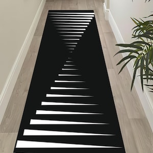May include: Black and white geometric runner rug. The rug features a repeating pattern of white lines against a black background, creating a visual illusion of depth. The rug is rectangular and designed for hallways or entryways.