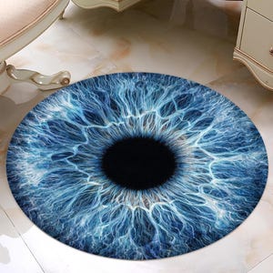 May include: A round rug featuring a detailed, artistic rendering of a human eye. The rug's design showcases a vibrant blue iris with intricate vein-like patterns radiating from a black pupil. The rug is a decorative floor covering.