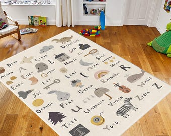 May include: A rectangular beige rug with the alphabet and corresponding illustrations. The rug features a dinosaur, house, rainbow, and zebra. The rug is placed on a wooden floor in a child's room.