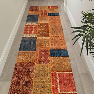 Peut inclure: Un long tapis de couloir rectangulaire présentant un motif patchwork composé de divers segments de tissu dans des tons de rouge profond, orange brûlé, jaune moutarde et bleu marine, chacun affichant des motifs floraux et géométriques.