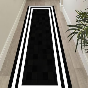May include: A rectangular black and white hallway rug. The rug features a black center with a checkered pattern, framed by a thick white border and a black outer edge. The rug is placed on a light-colored wooden floor.