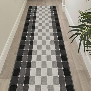 May include: A long rectangular runner rug featuring a repeating geometric pattern of rounded squares in shades of black, charcoal gray, and light gray. The design includes small white accents between the squares, creating a grid-like effect.