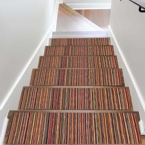 May include: A set of rectangular stair treads featuring a vertical striped pattern in shades of orange, red, yellow, blue, and brown. The treads are installed on wooden stairs with white walls on both sides, creating a colorful and textured look.