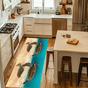 May include: A kitchen rug with a blue and beige design featuring two sea turtles swimming in the ocean. The rug is placed on a wooden floor in front of white kitchen cabinets.